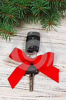 Car key with red ribbon bow on white natural wooden table background. Christmas or Valentine`s Day gift or present abstract conce