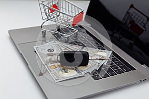 Car keys with dollar banknotes and shopping cart on a laptop. Online purchase car concept