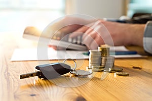 Car keys and money on table with man using calculator.