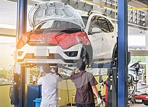 Car on lift to repair suspension in the garage with mechanics working underneath lifted car to change wheel hub