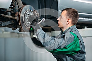 Car lifted in automobile service for fixing, worker repairs the wheel,