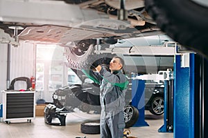 Car lifted in automobile service for fixing, worker repairs the wheel,