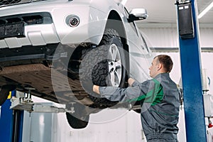 Car lifted in automobile service for fixing, worker repairs the wheel,