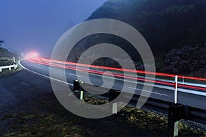 Car light trails on a foggy road at night