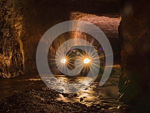 Car lights and flare inside deep old mining tunnel cave with reflection. rock wall cave with water lodge rocky road. adventure