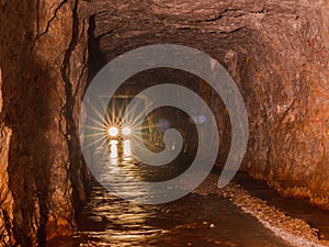 Car lights from inside deep old mining tunnel cave with reflection. rock wall cave with water lodge rocky road. adventure travel