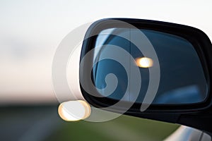 Car lights reflecting in the side mirror of a car parked on the curb of a highway