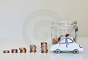 Car loan, car insurance concept. Glass jar full of coins, stacks of coins and white paper car