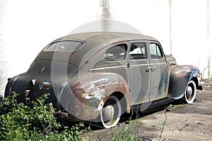 This old car is rusting and deteriorating by the wall. photo
