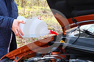 Car maintenance concept. Filling windshield washer fluid on car. Driver with washer fluid in his hands, close up