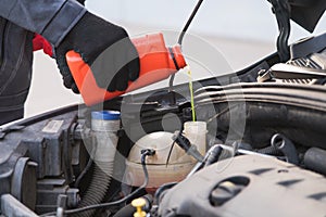 Car master mechanic pouring antifreeze into expansion tank at car service workshop