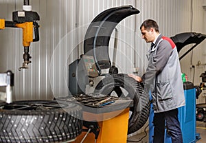 Car mechanic balancing car wheel on balancer in auto repair service.