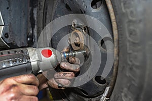 The car mechanic bolts the steel car wheel with a pneumatic wrench in a car workshop, visible male hands.