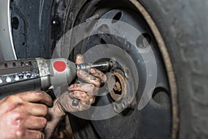The car mechanic bolts the steel car wheel with a pneumatic wrench in a car workshop, visible male hands.