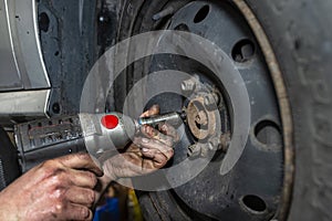 The car mechanic bolts the steel car wheel with a pneumatic wrench in a car workshop, visible male hands.