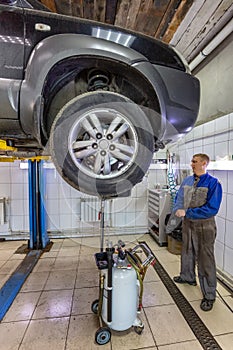 Car mechanic changes oil in a workshop. Mechanic standing next to the car and draining oil into a special cannister. Car is on the