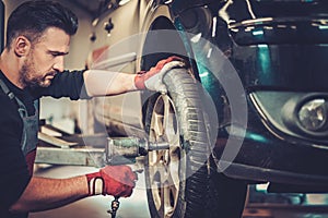 Car mechanic changing car wheel in auto repair service.