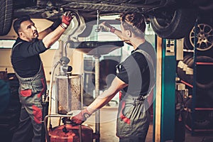 Car mechanic changing motor oil in automobile engine at maintenance repair service station in a car workshop.