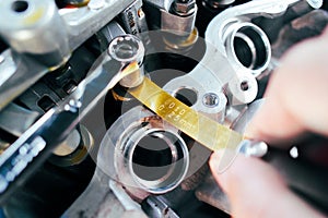 Car mechanic checking and adjusting valves of car engine with feeler gauge or thickness gauge tool