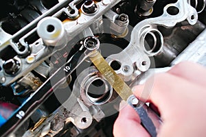 Car mechanic checking and adjusting valves of car engine with feeler gauge or thickness gauge tool