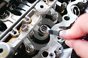 Car mechanic checking and adjusting valves of car engine with a ring wrench