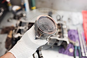 Car mechanic in garage with old car engine piston.