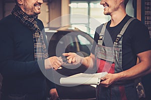 Car mechanic giving client keys to his repaired car in auto repair service.