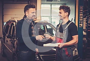 Car mechanic giving client keys to his repaired car in auto repair service.