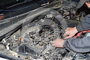 A car mechanic in a gray uniform and cap unscrews the fuel ramp on the engine