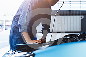 Car mechanic holding clipboard and checking to maintenance vehicle by customer claim order in auto repair shop garage. Engine