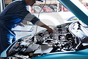 Car mechanic holding clipboard and checking to maintenance vehicle by customer claim order in auto repair shop garage. Engine