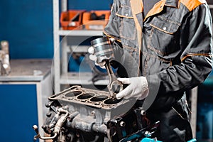 Car mechanic holding a new piston for the engine, overhaul.. Engine on a repair stand with piston and connecting rod of