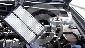 Car mechanic holds car air filter in hands near engine compartment, plans to replace old filter, close-up. Concept