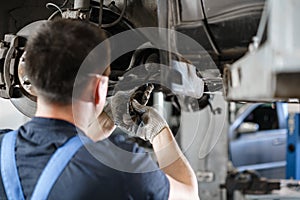 Car mechanic inspecting car wheel and repair suspension detail. Lifted automobile at repair service station. replacement