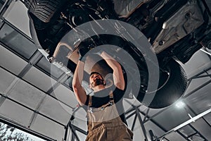 Car mechanic inspecting car wheel and suspension detail of lifted automobile at repair service station