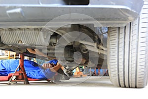 Car mechanic lying down and working under car in auto repair service