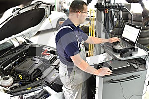 Car mechanic maintains a vehicle with the help of a diagnostic computer - modern technology in the car repair shop