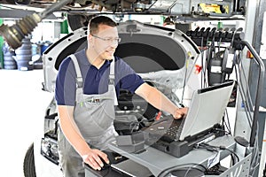 Car mechanic maintains a vehicle with the help of a diagnostic computer - modern technology in the car repair shop