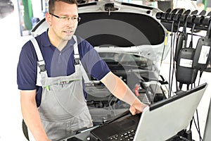 car mechanic maintains a vehicle with the help of a diagnostic computer - modern technology in the car repair shop photo