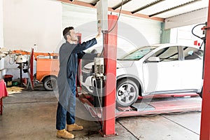 Car Mechanic Operating Hydraulic Lift In Repair Shop