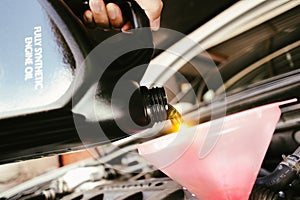 A car mechanic is pouring new engine oil into a funnel into the car engine