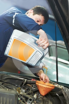 Car mechanic pouring oil into motor engine