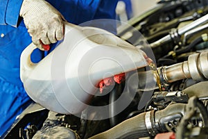 Car mechanic pouring oil into motor engine