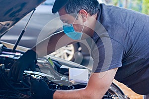 Car mechanic on protective mask fixing car engine, auto mechanic is repairing car engine