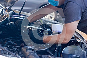 Car mechanic on protective mask fixing car engine, auto mechanic is repairing car engine