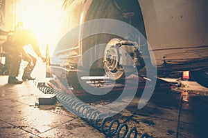 Car mechanic replace car wheels of lifted automobile by pneumatic wrench at repair service shop garage station, sunlight effect