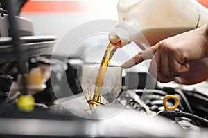 Car mechanic replacing and pouring fresh oil into engine at maintenance repair service station