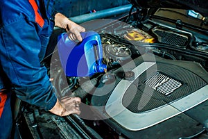 Car mechanic replacing and pouring oil into engine at maintenance repair service station.