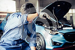 Car mechanic resting from exhaustion and wiping sweat from tired hard work in auto repair shop garage. Business industry and