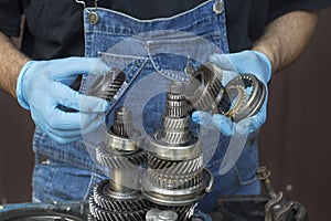 Car mechanic in rubber gloves holds in his hands gears and modes from a mechanical gearbox. Repair of manual transmission in a car